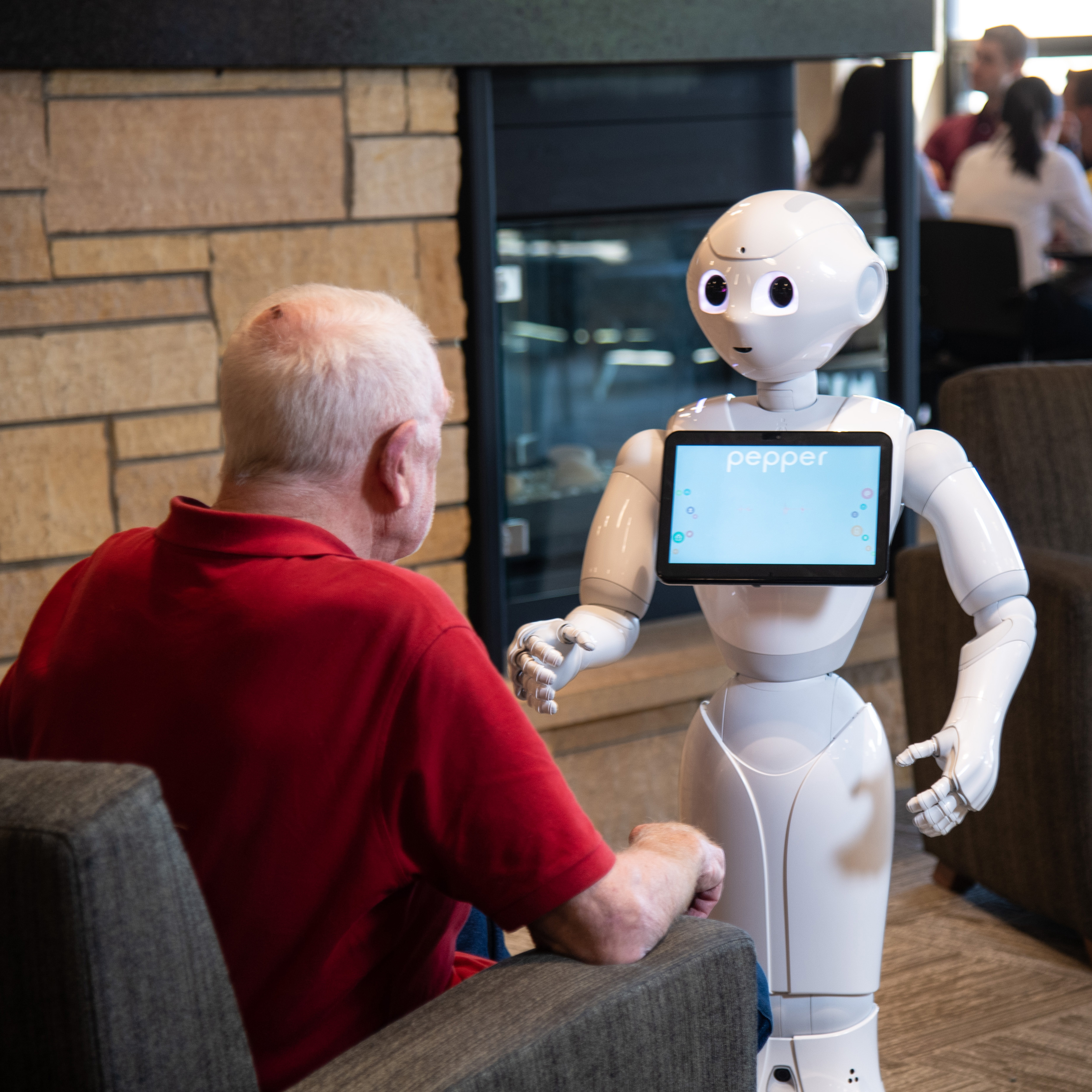 A senior citizen wearing a red shirt interacts with Pepper the robot. 