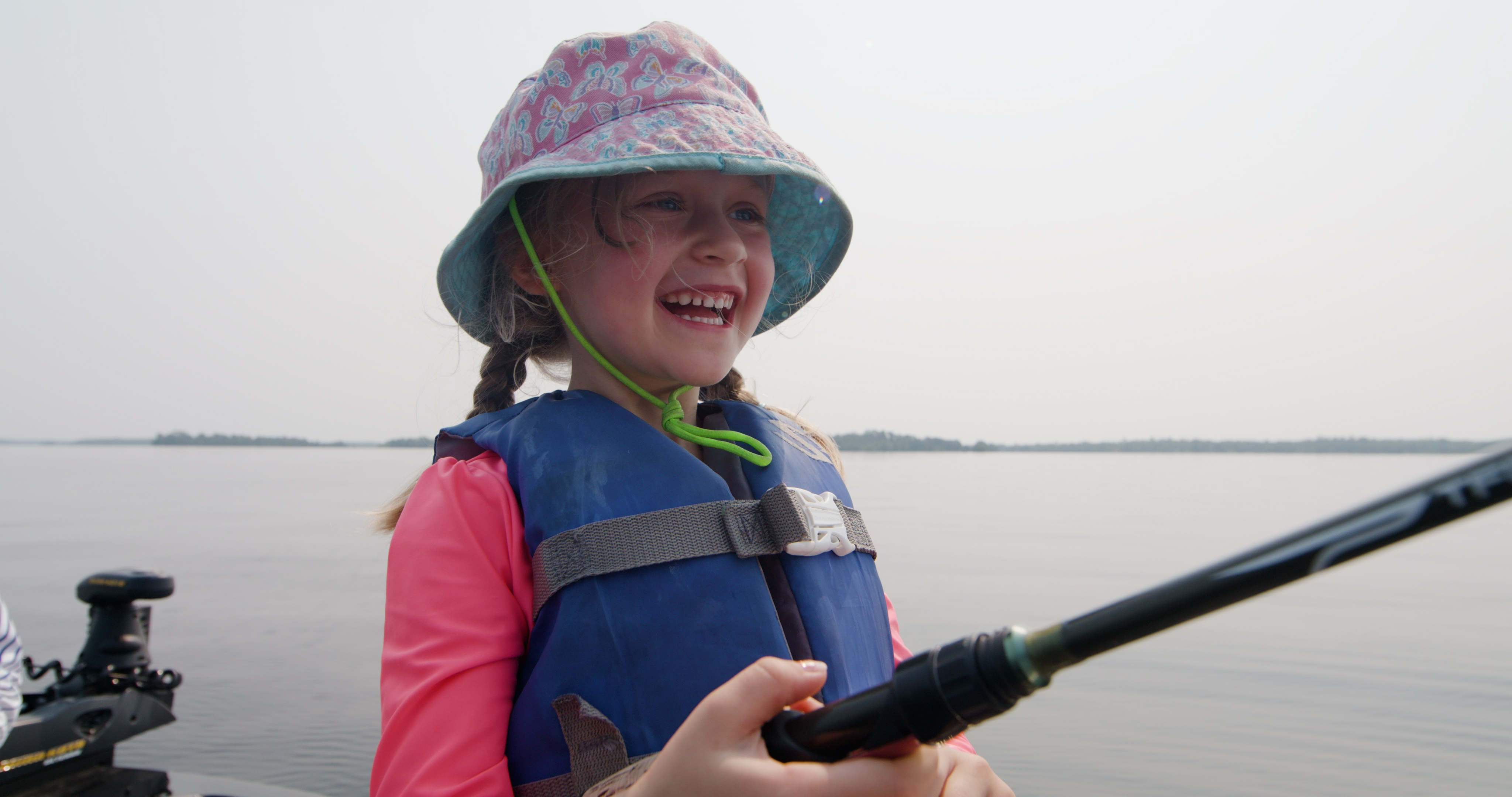 A small child wearing a life vest on a boat and fishing
