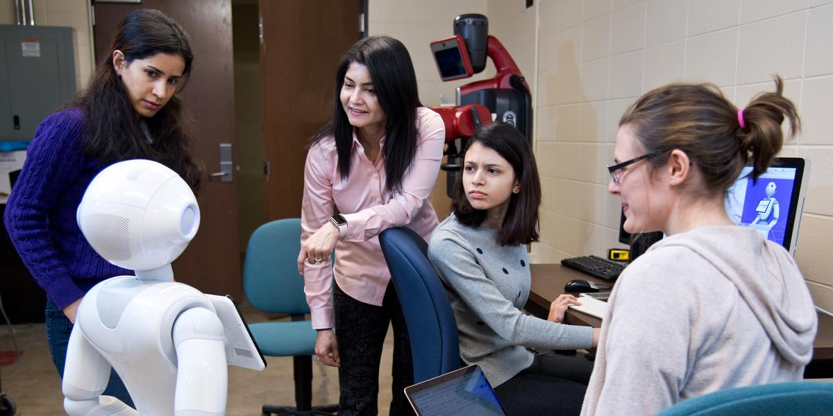 Dr. Arshia Khan and three students gather around Pepper, a robot. 