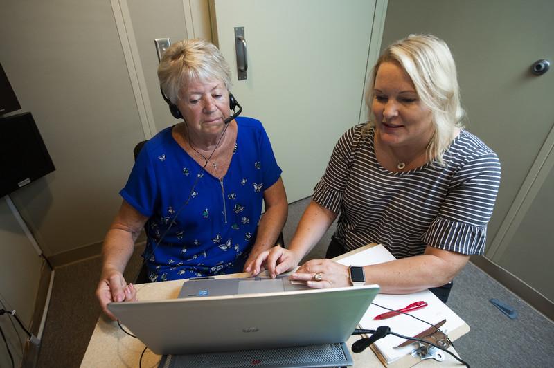 Two women sitting in front of a laptop. One of them is wearing a headset.